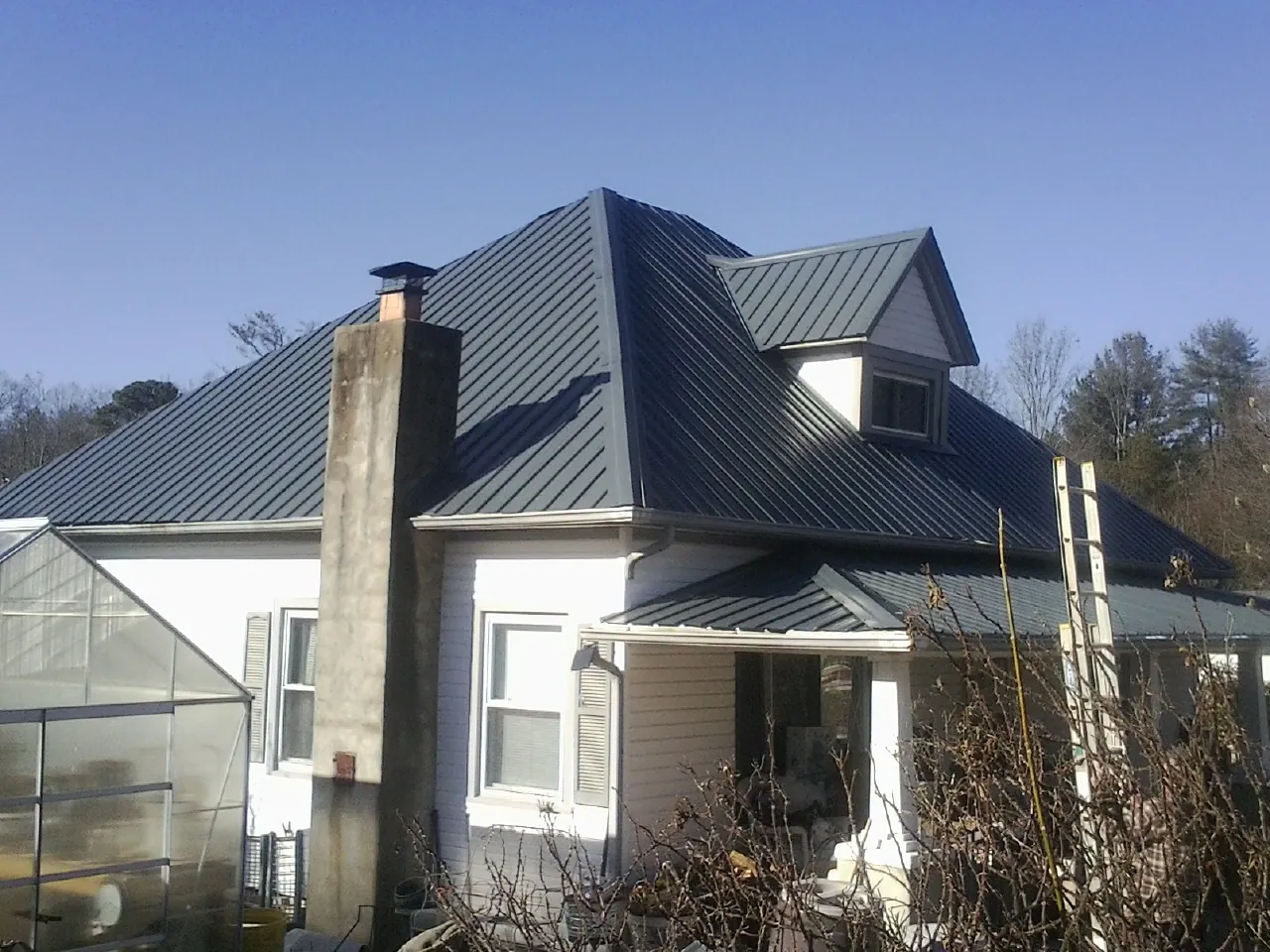 Dark blue standing seam metal roof on a white farmhouse with dormer — Slate & Tile Roof Repair by Roofing Brothers in Valrico