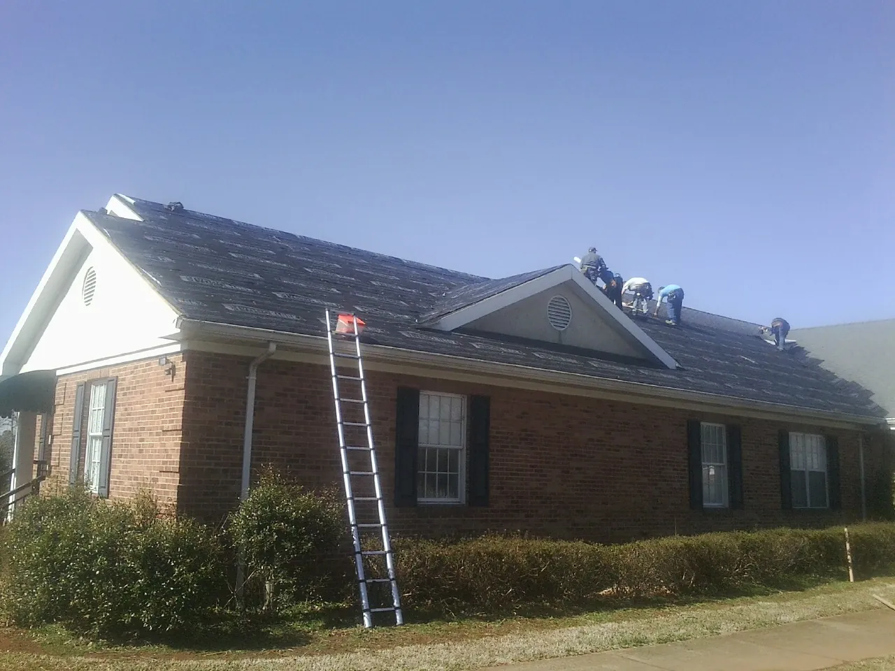 Crew tearing shingles off a brick ranch roof with a ladder set — Metal Roof Repair work by our crew in Valrico