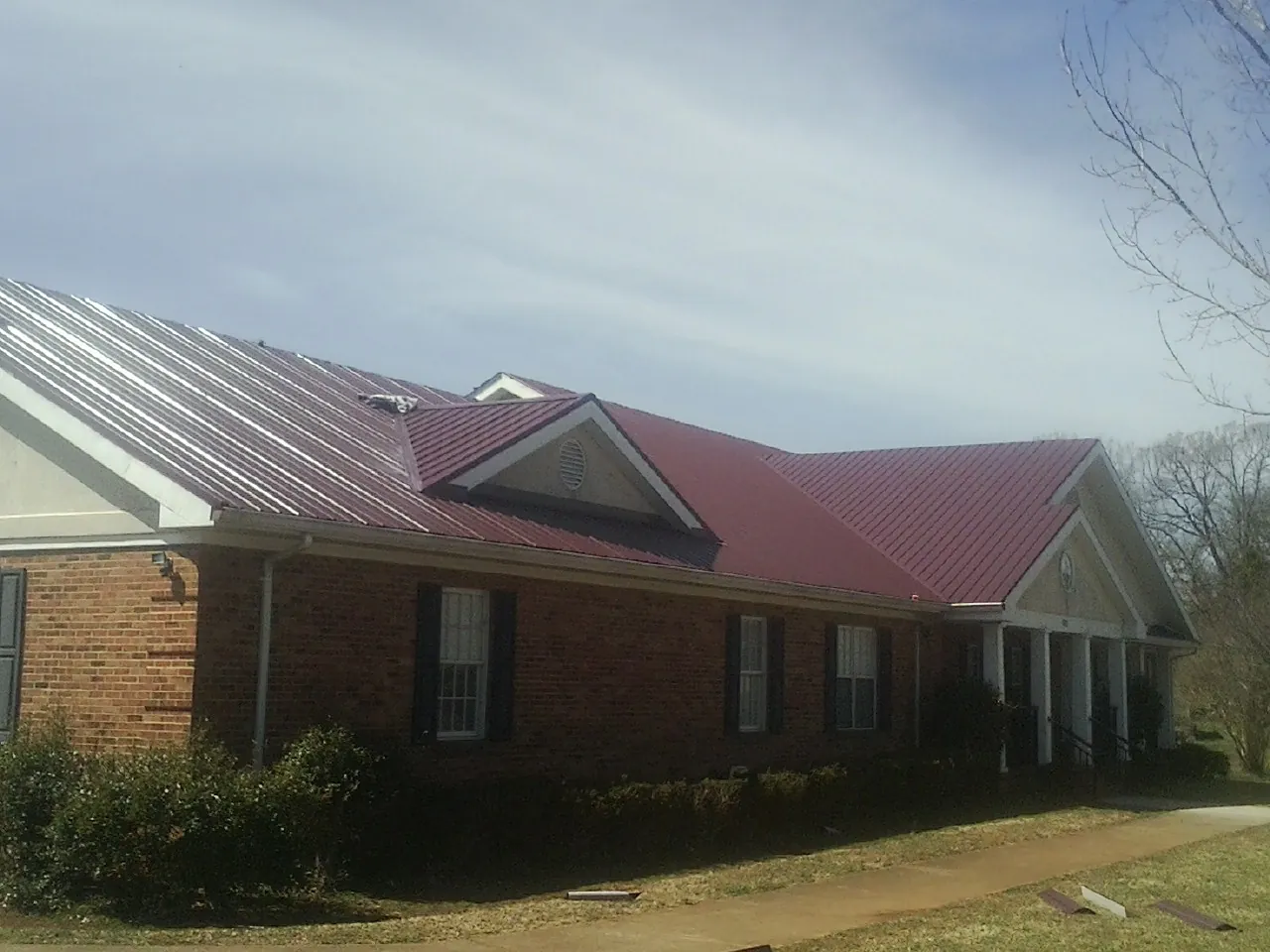 Red metal roof with gabled entries on a long brick building, from a Hail Damage Roof Repair job in Valrico
