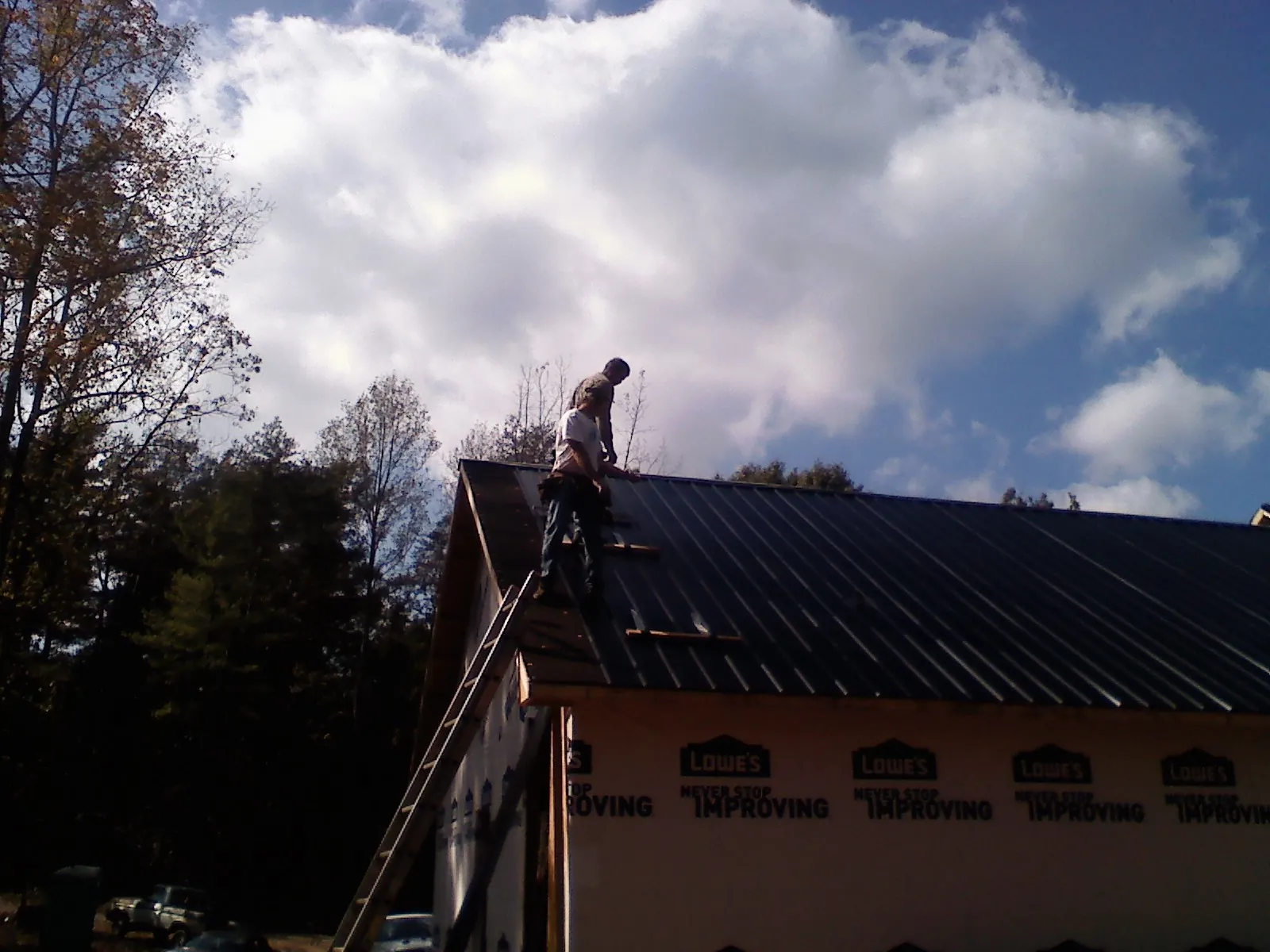 Roofer fastening dark metal panels high against a cloudy sky, from a Roof Inspection job in Valrico