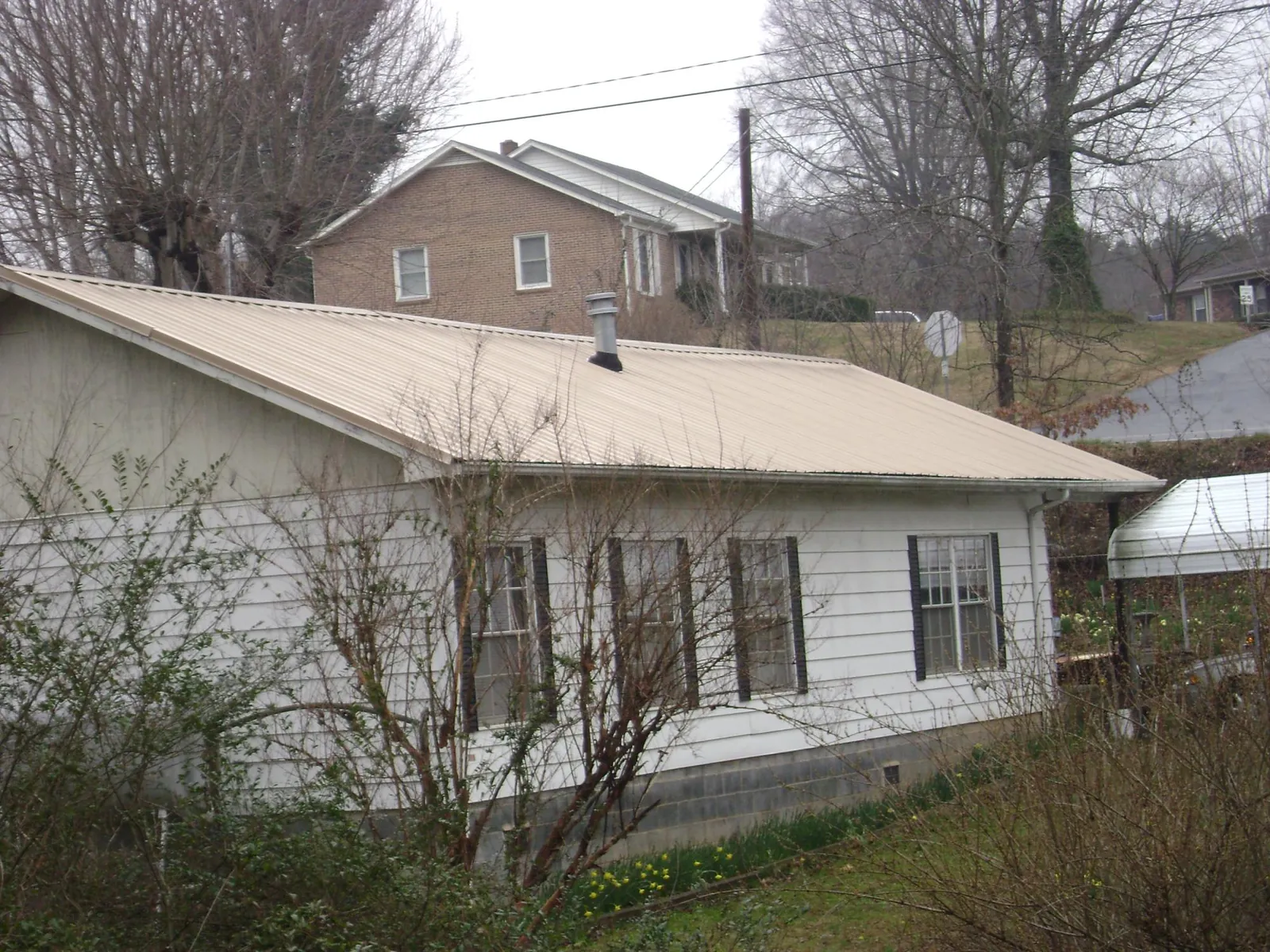 Tan metal roof on a white sided house set into a hillside — Commercial Roofing by Roofing Brothers in Valrico