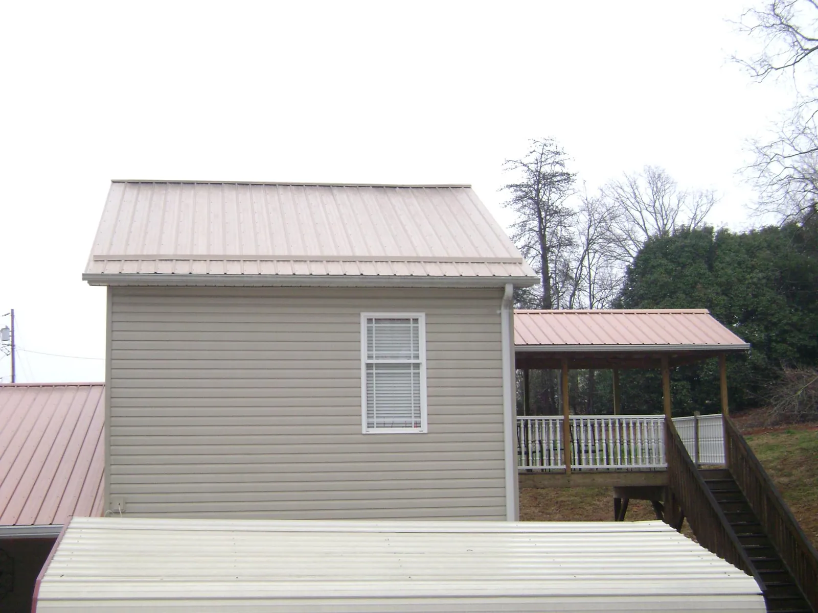 Tan metal roofs on a two story addition and attached porch, from a Roof Replacement job in Valrico